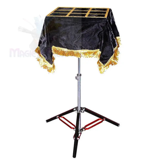 Ein Zaubertisch aus schwarzem Samt mit goldenen Fransen und einer segmentierten Platte, die von einem schwarz-silbernen Stativ getragen wird.