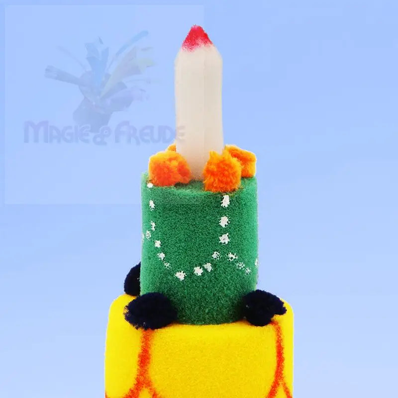 Eine festliche, mehrschichtige Kuchendekoration in Form einer Kerze auf einem grünen Boden mit orangefarbenen Bommeln, die auf einer gelben Schicht mit schwarzen Bommeln und orangefarbenen Zierlinien sitzt.