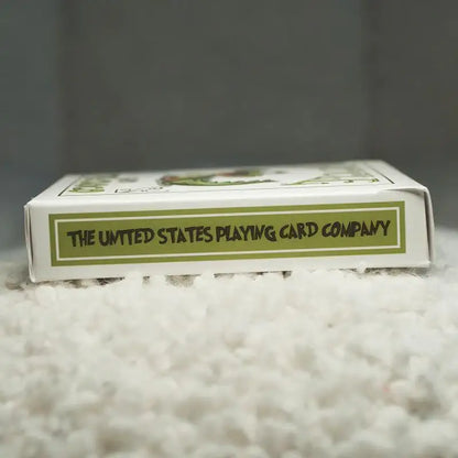 Weiße Kartenschachtel mit Aufschrift 'The United States Playing Card Company' auf grünem Hintergrund, liegend auf Teppich.