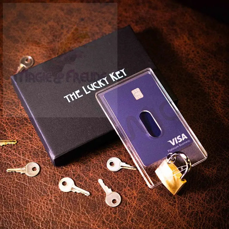 Ein schwarzes Kästchen mit der Aufschrift ’THE LUCKY KEY’ mit einer lila Visa-Karte in einem durchsichtigen Halter und einem kleinen goldenen Vorhängeschloss, umgeben von mehreren kleinen silbernen Schlüsseln.