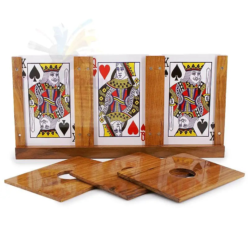Ein hölzerner Zaubertrickapparat mit drei Spielkarten (zwei Pik-Könige, eine Herz-Dame) und drei abnehmbaren Holzplatten mit kreisförmigen Aussparungen.