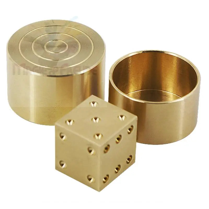 Ein Würfelspiel aus Messing mit einem massiven Würfel und zwei zylindrischen Behältern.