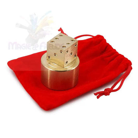 Ein würfelförmiges Puzzle oder Zaubertrickrequisit aus Messing mit zylindrischer Basis, das auf einem roten Kordelzugbeutel ruht.