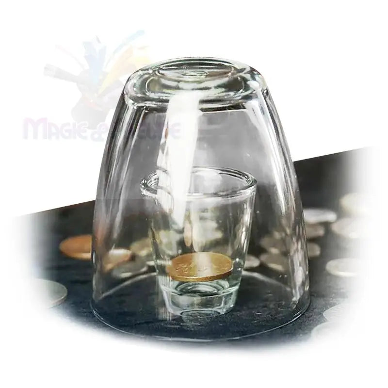 Ein klares Glas, das auf ein Schnapsglas mit Wasser und einer Münze gestülpt wird.