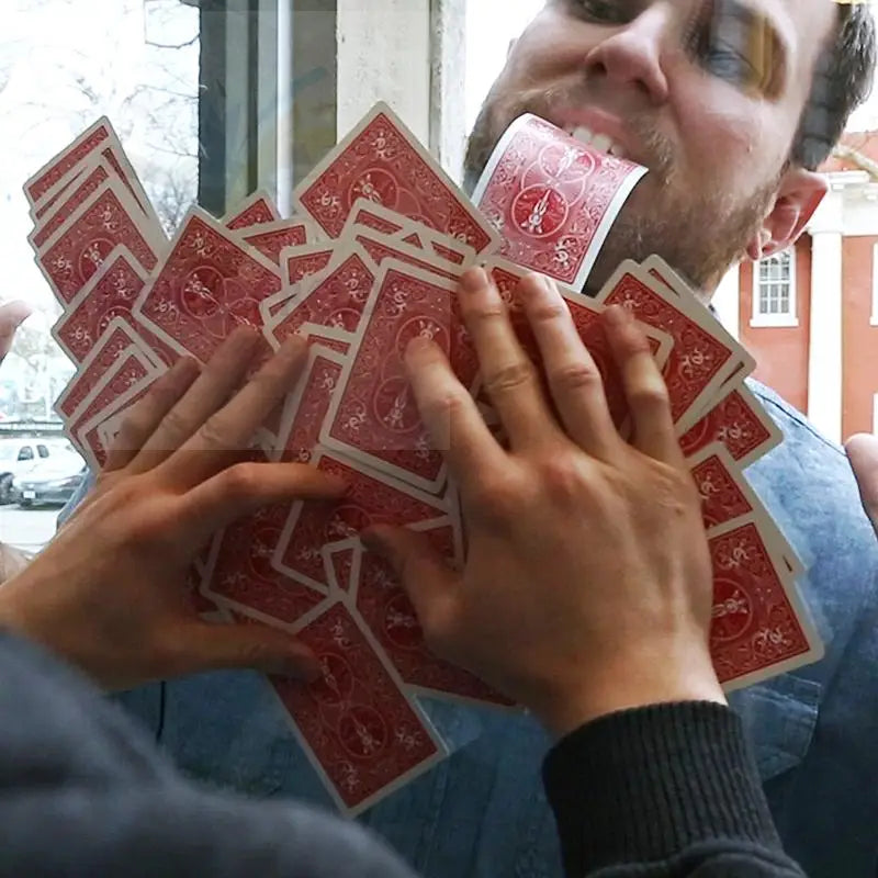 Ein Mann mit einem Mund voller roter Spielkarten, die von zwei Händen gehalten werden.