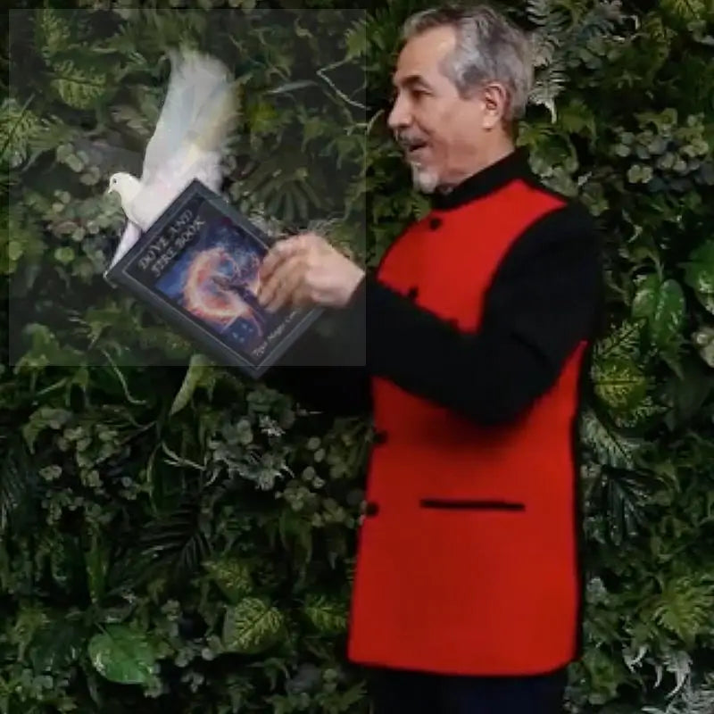 Ein Mann in roter Weste hält ein Buch mit einem bunten Einband in der Hand, daneben eine weiße Taube.