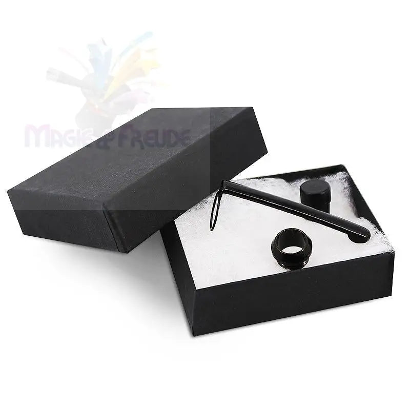 Eine geöffnete schwarze Geschenkschachtel, die einen schwarzen stiftähnlichen Gegenstand, einen Ring und eine kleine zylindrische Kappe enthält.