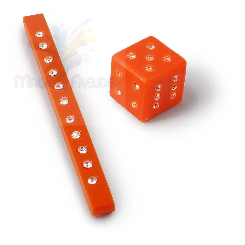 Ein orangefarbenes Kunststofflineal und ein passender Würfel, beide mit funkelnden, klaren Strasssteinen verziert.