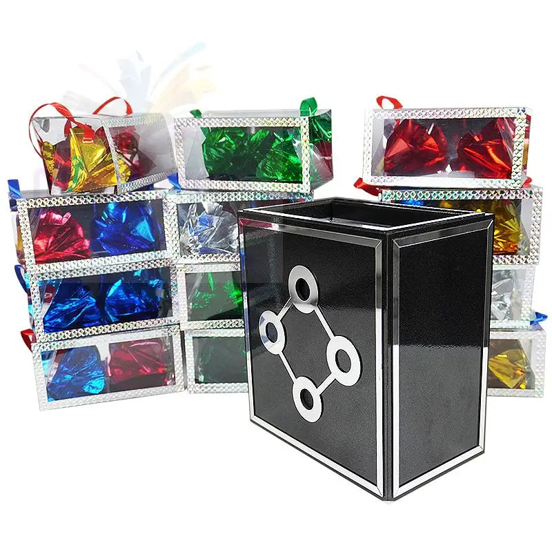 Eine schwarze rechteckige Schachtel mit einem silbernen geometrischen Muster, umgeben von durchsichtigen Geschenkschachteln, die bunt verpackte Süßigkeiten enthalten.