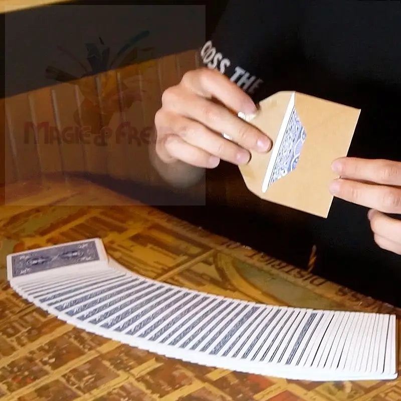 Ein auf einem Tisch aufgefächertes Kartenspiel mit einer Hand, die eine einzelne Karte hält, die teilweise in einen kleinen, hellbraunen Umschlag gesteckt ist.