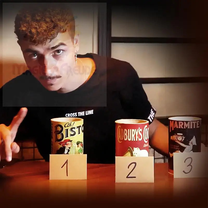 Ein junger Mann mit Schnurrbart und lockigem Haar, der ein schwarzes T-Shirt trägt, steht hinter drei nummerierten Lebensmitteldosen.