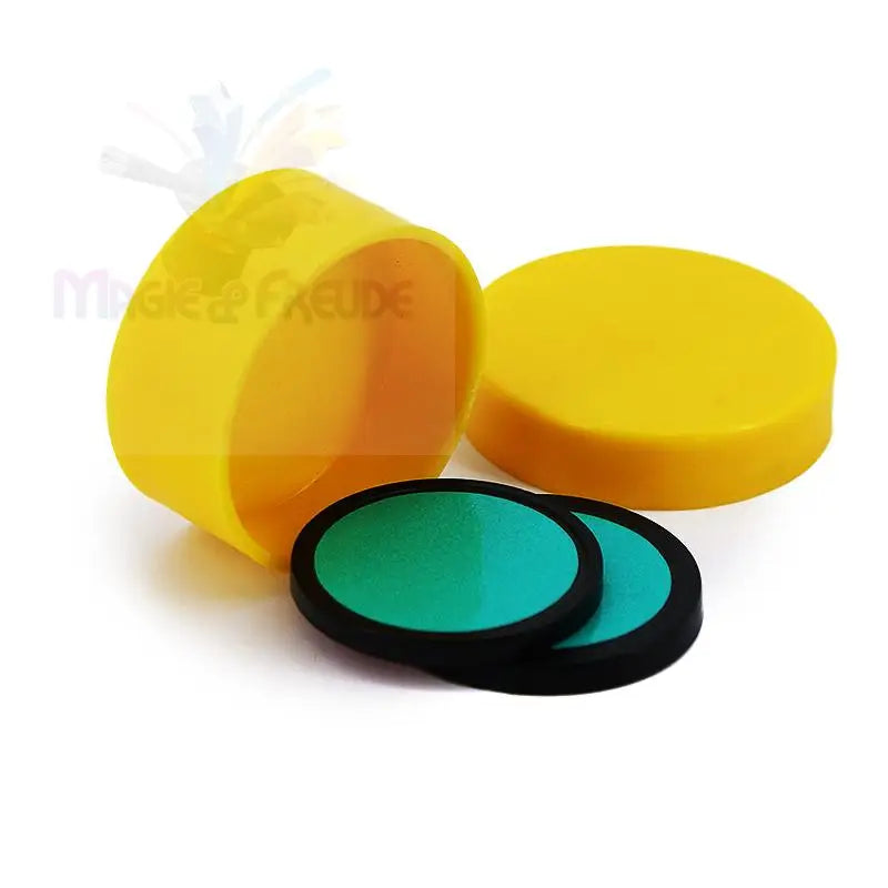 Zwei grüne Rundfilter mit schwarzem Rand, daneben ein offener gelber Behälter mit Deckel.