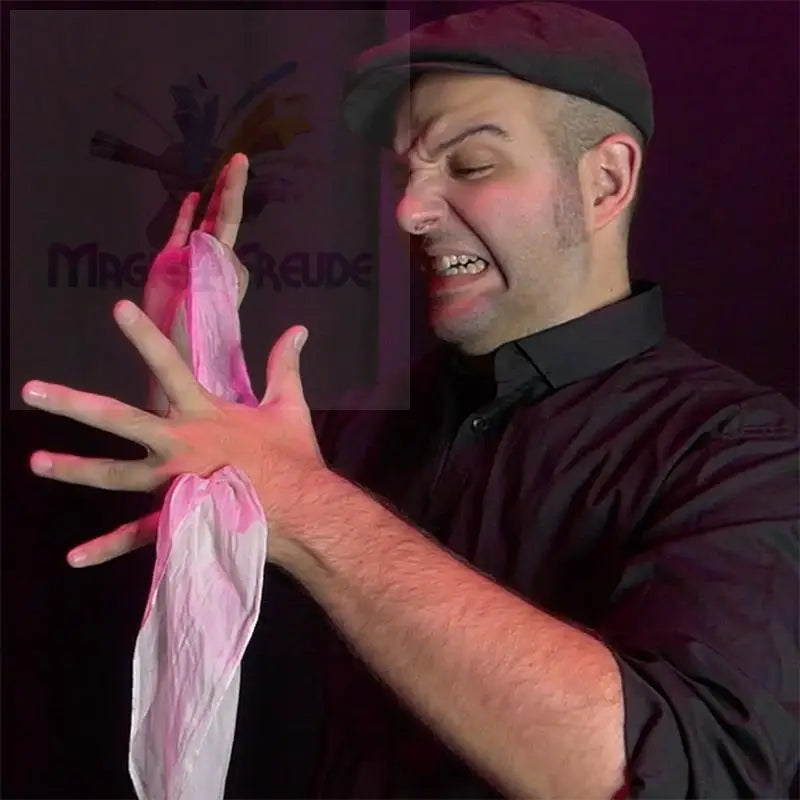 Mann mit flacher Mütze und schwarzem Hemd, der eine Grimasse zieht und zwei rosa, zerknitterte Tücher in den Händen hält.