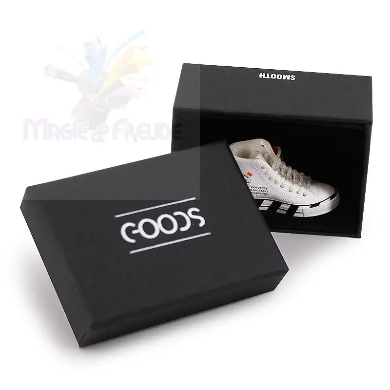 Ein kleiner weißer High-Top-Sneaker mit schwarzen Streifen und roten Akzenten, ausgestellt in einer offenen schwarzen Schachtel.