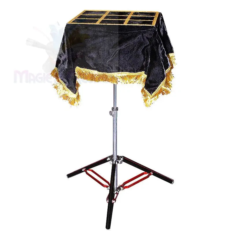 Ein tragbarer Tisch für Zaubertricks mit einem schwarz-goldenen Fransentuch, einer gitterförmigen Platte und einem zusammenklappbaren Stativ.